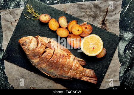 Grilled whole fish Served with baked potatoes, lemon and sauce. Top view. Stock Photo