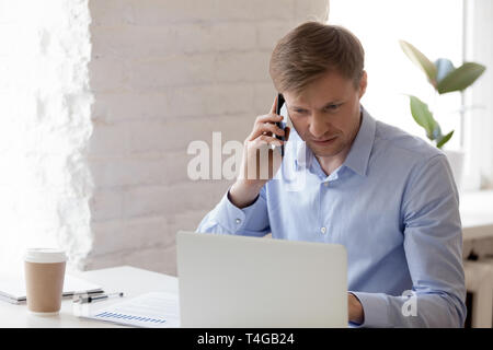 Manager working on laptop and talking at smartphone Stock Photo