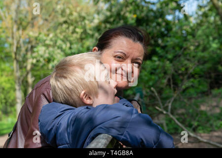 Defect,childcare,medicine and people concept: Happy mother and son with down syndrome playing together in a park at spring time. Stock Photo