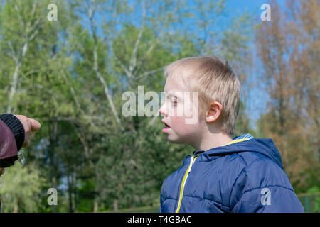 Defect,childcare,medicine and people concept: Happy mother and son with down syndrome playing together in a park at spring time. Stock Photo