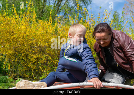 Defect,childcare,medicine and people concept: Happy mother and son with down syndrome playing together in a park at spring time. Stock Photo