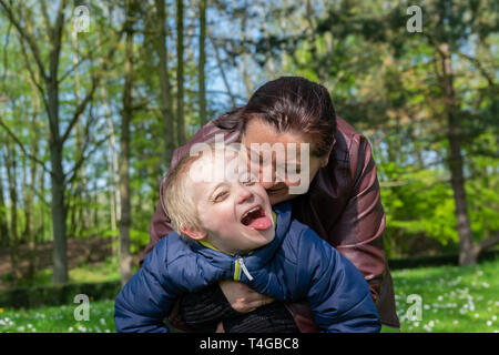 Defect,childcare,medicine and people concept: Happy mother and son with down syndrome playing together in a park at spring time. Stock Photo