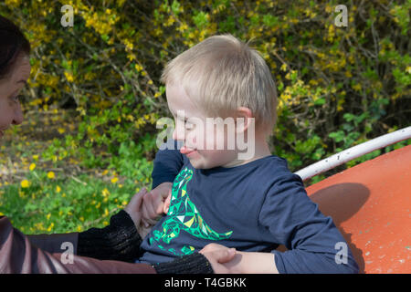 Defect,childcare,medicine and people concept: Happy mother and son with down syndrome playing together in a park at spring time. Stock Photo