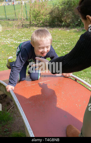 Defect,childcare,medicine and people concept: Happy mother and son with down syndrome playing together in a park at spring time. Stock Photo