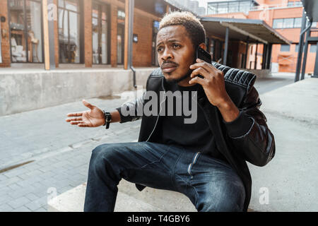 Dark-skinned unpleasantly surprised and annoyed man talking by mobile phone. Stock Photo