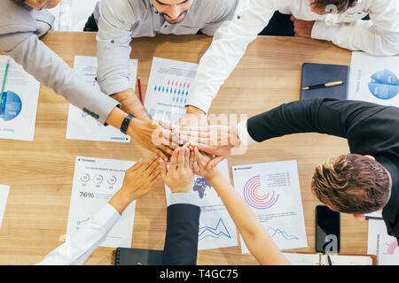 Crop coworking business people stacking hands above wooden desk with paper documents Stock Photo
