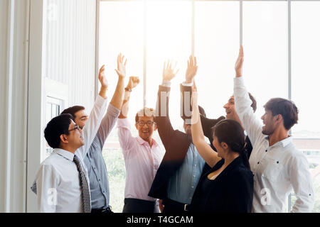 Group of multiethnic business men and woman raising hands up giving high five in sunny office Stock Photo