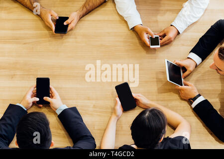 Crop from above of formal business men and women sitting in circle at table and using mobile phones in office Stock Photo