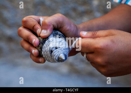 A boy rolling the string in a wooden spinning top on the road. Old Turkish traditional toy. Stock Photo