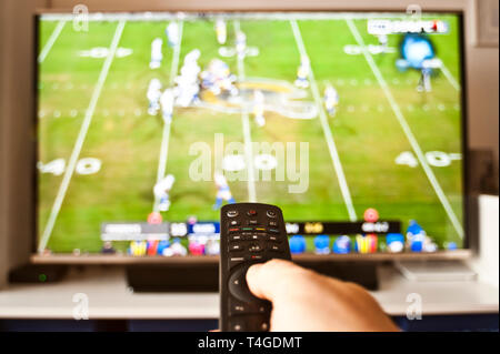 hand holding remote control in front of tv on a sport channel Stock Photo