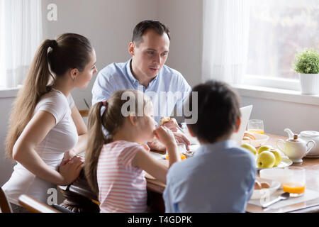 Parents watching computer while children eating breakfast at kitchen Stock Photo