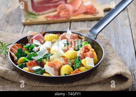 Fried Italian gnocchi with fresh spinach leaves, crispy roasted South Tyrolean bacon and parmesan cheese served in a frying pan Stock Photo