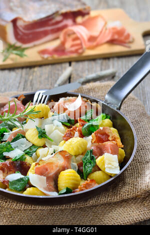 Fried Italian gnocchi with fresh spinach leaves, crispy roasted South Tyrolean bacon and parmesan cheese served in a frying pan Stock Photo