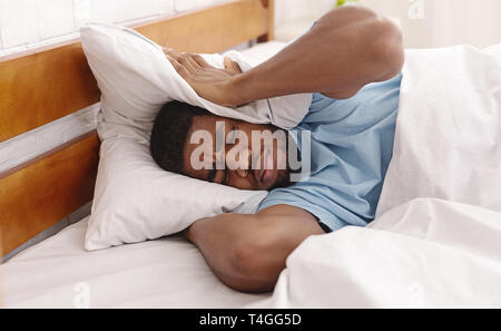 Young man in bed hiding under pillow Stock Photo