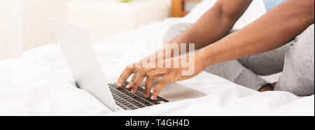 African-american programmer typing on laptop in bed Stock Photo
