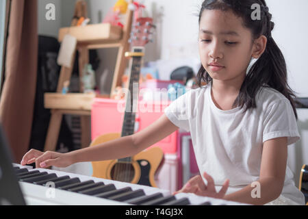 Asian little girl learning to play piano keyboard synthesizer with happiness, Thai girl studying the music at home Stock Photo
