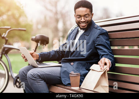 African businessman using laptop and having lunch outdoors Stock Photo