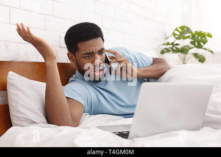Angry man having problems with laptop talking on mobile phone Stock Photo