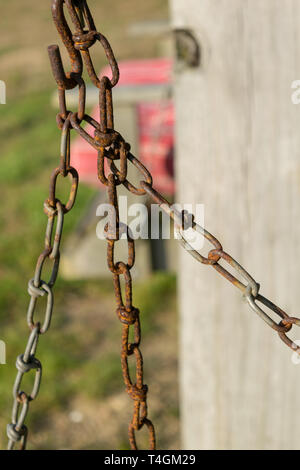 Old rusty chain and chain links against a bokeh wooden pole and pink seat in the background, Block Island, RI Stock Photo
