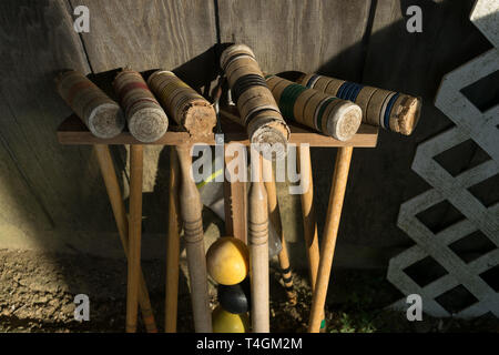 Old well-used Croquet mallets in a rack, leaning against a wooden wall, at a downward angle Stock Photo