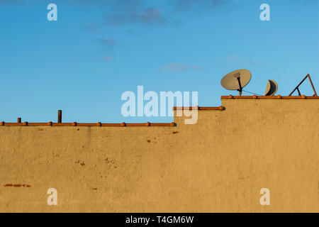 Empty painted brick wall and terracotta clay roofing tile shingles and a couple of old satellite TV receiver dishes during golden hour, Bronx, NY, USA Stock Photo
