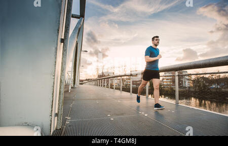 Running man runner training doing outdoor city run sprinting over a bridge. Urban healthy active lifestyle. Male athlete running over sunset backgroun