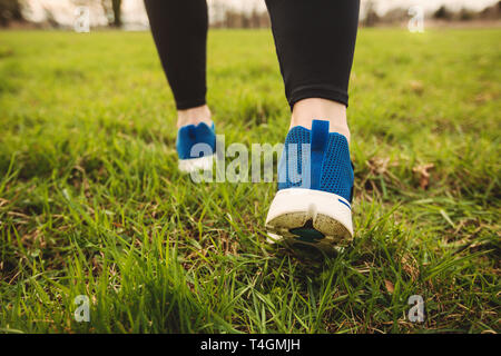 Athletic pair of legs running on grass during sunset city park. Stock Photo