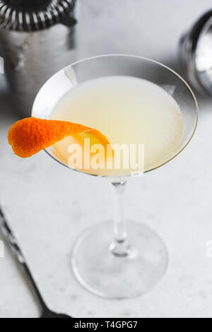 Corpse Reviver No. 2 classic Cocktail with orange peel surrounded by metal bar tools on a white table. Stock Photo