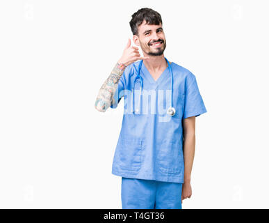 Young handsome nurse man wearing surgeon uniform over isolated background smiling doing phone gesture with hand and fingers like talking on the teleph Stock Photo