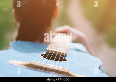 teenage girl walking outdoors carrying acoustic denim guitar on her shoulder Stock Photo