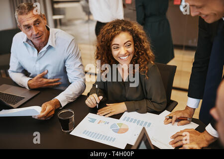 Smiling young businesswoman going over graphs with colleagues during a meeting in an office boardroom Stock Photo