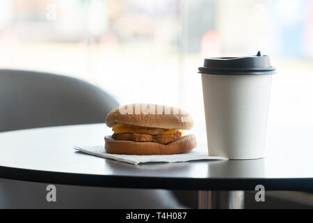 Bacon and Omelette Hamburger on the paper with White paper coffee mug on the table in fast food restaurant Stock Photo