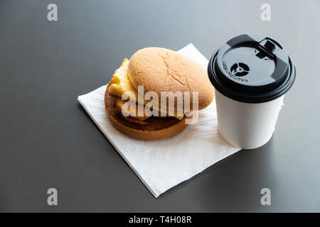 Bacon and Omelette Hamburger on the paper with White paper coffee mug on the table in fast food restaurant Stock Photo