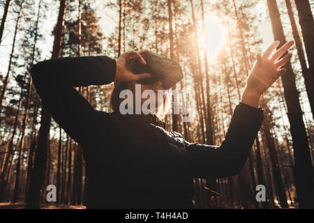 Woman in forest with virtual reality headset looking straight and trying to touch something with her hand Stock Photo