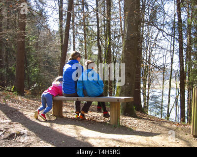 Happy mother with son and daughter sitting on a bench and looking at a beautiful forest view Stock Photo
