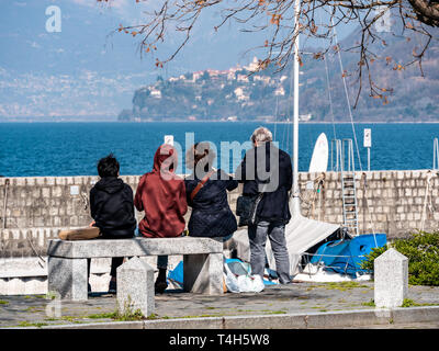 Image of family sitting on a stone bench from behind with lake maggiore in the background Stock Photo