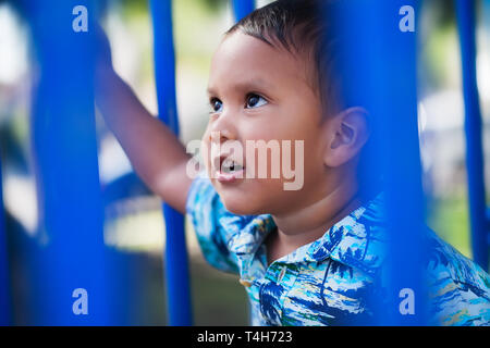 Cute little boy wearing a hawaiin print shirt and looking up with a positive facial expression while playing in an outdoor kids playground. Stock Photo