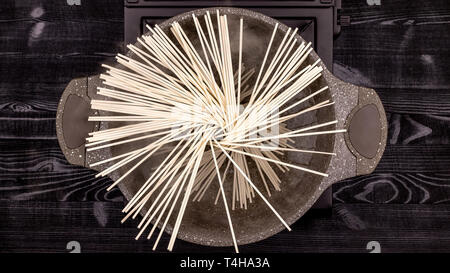 Flat noodles boiled in boiling water in a saucepan with a stone coating and scattered in a circle in the form of a fan around the circumference Stock Photo