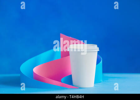 Blank paper cup for coffee on an abstract background with modern paper sculpture. Paper pyramids and curves design in pastel colors. Stock Photo