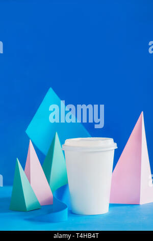 Blank paper cup for coffee on an abstract background with modern paper sculpture. Paper pyramids and curves design in pastel colors. Stock Photo