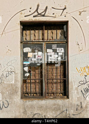 Manila, Philippines - January 17, 2017: Metal window frame with broken glass, rusty welded grills in a very dirty wall with stickers and graffiti Stock Photo