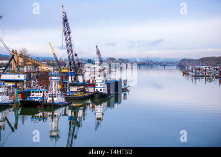 Industrial pier with floating docks on the Columbia River, moored river tugs, cranes for unloading and loading barges on one side and floating houses  Stock Photo