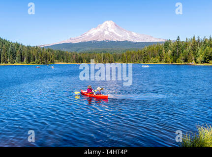 Man and woman in hats ride kayak on the Trillium Lake overlooking Mount Hood with the reflection of snowy mountain in the clear water of the lake cove Stock Photo