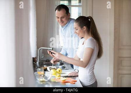 Happy young couple watching video on smartphone while cooking Stock Photo