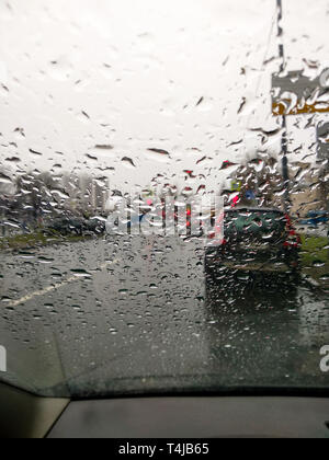 Raindrops on the windshield. View from inside the car. Red traffic signal. Cityscape. Stock Photo
