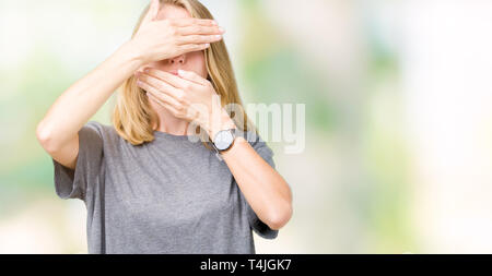 Beautiful young woman wearing oversize casual t-shirt over isolated background Covering eyes and mouth with hands, surprised and shocked. Hiding emoti Stock Photo