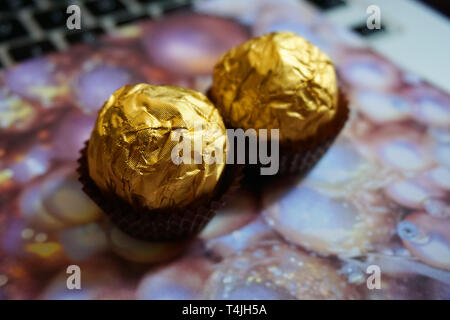 chocolate ball milk hazelnut chocolate wrapped in gold and brow packaging with pink Christmas background dessert beautiful blurred background Stock Photo
