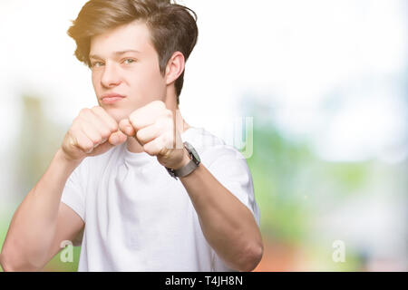 Young handsome man wearing casual white t-shirt over isolated background Punching fist to fight, aggressive and angry attack, threat and violence Stock Photo