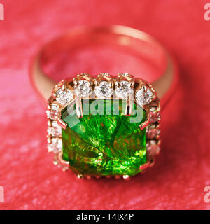 The Golden Ring with a big emerald and a path from small cubic zirconias on a red abstract background, a close up Stock Photo