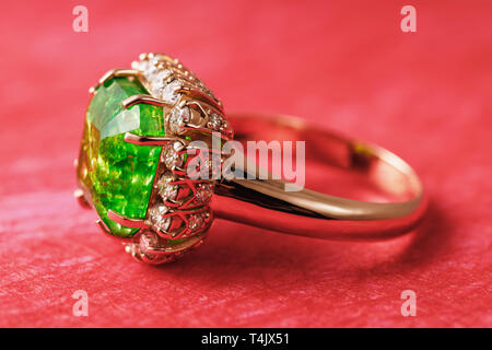 Golden ring with a large emerald and a path of small cubic zirconias on a red abstract background, side view Stock Photo